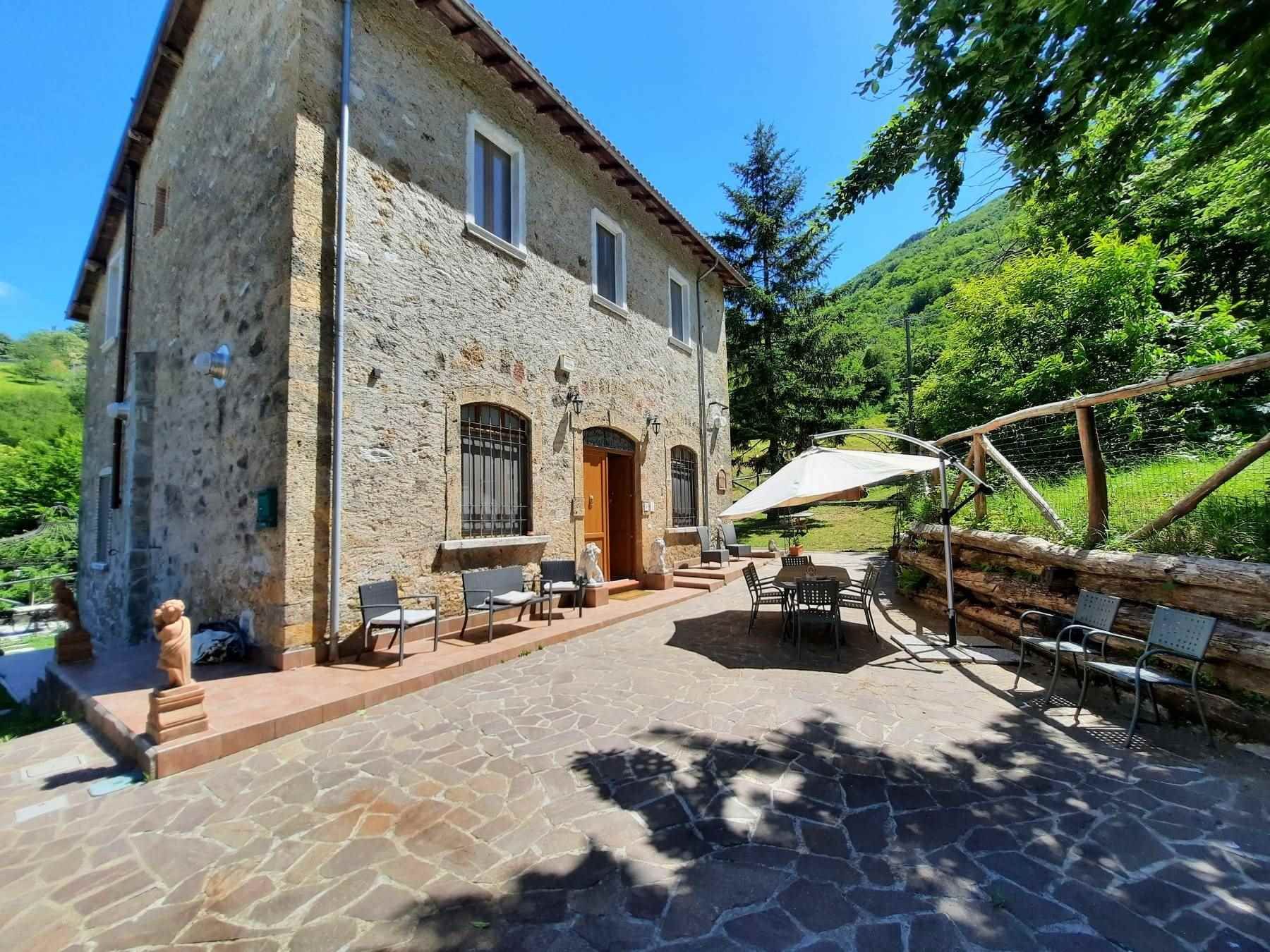 Stone façade of Cava House with its terrace and summer greenery